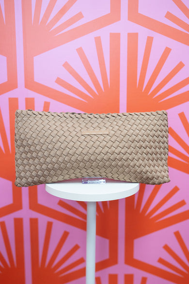 Beige woven mahjong tile bag on a white stand against a pink and orange geometric patterned background