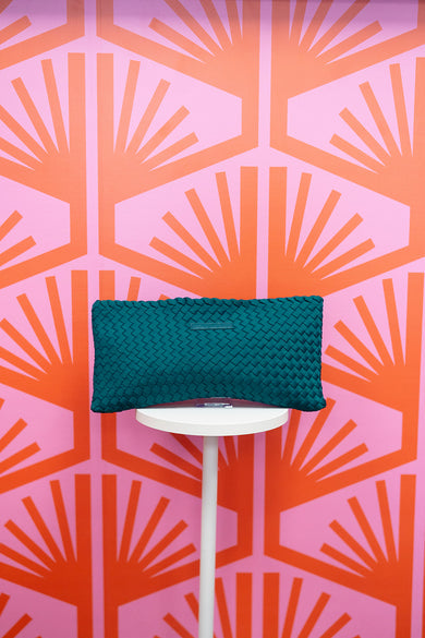 Teal woven mahjong tile bag on a white stand against a pink and orange geometric patterned background
