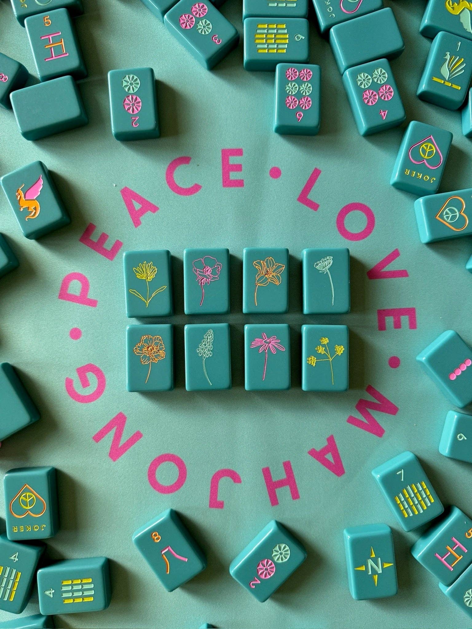 Teal Mahjong tiles with pink 'Peace Love Mahjong' text on a green background