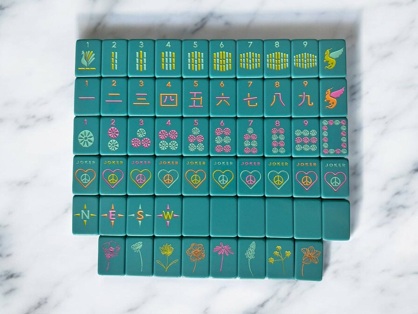 Set of teal mahjong tiles with colorful symbols on a marble surface