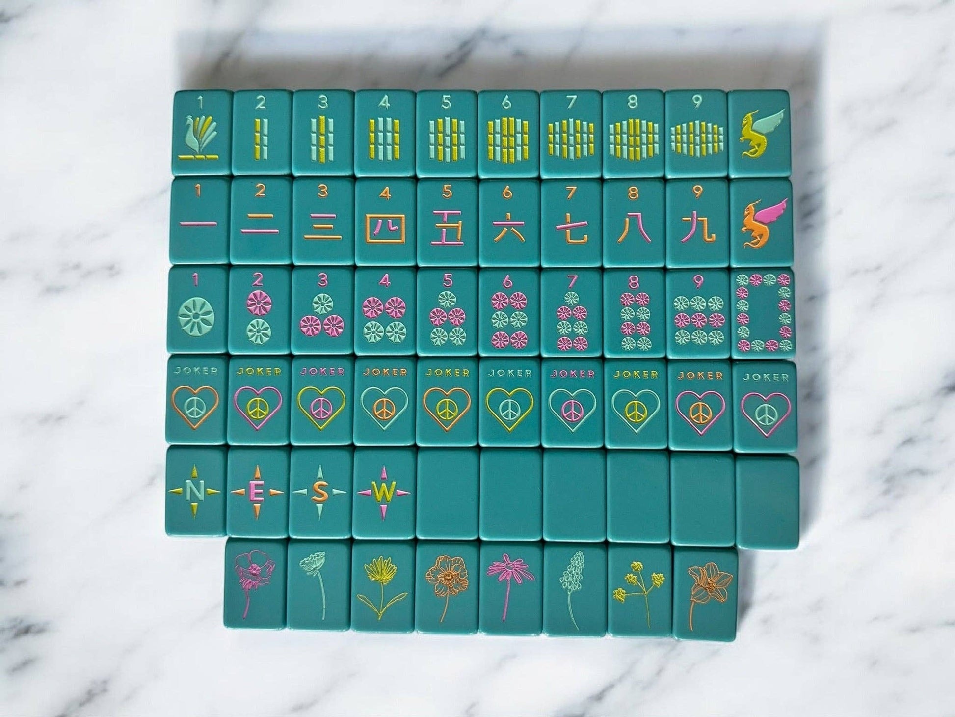 Set of teal mahjong tiles with colorful symbols on a marble surface
