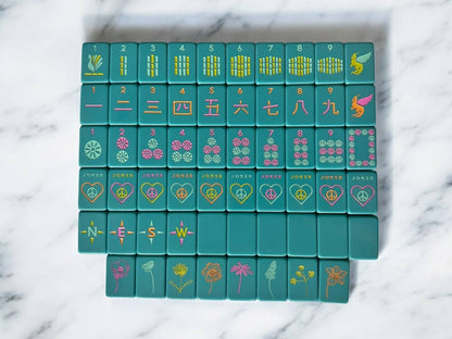 Set of teal mahjong tiles with colorful symbols on a marble surface