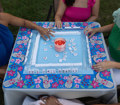 People playing mahjong on a floral-patterned mat outdoors